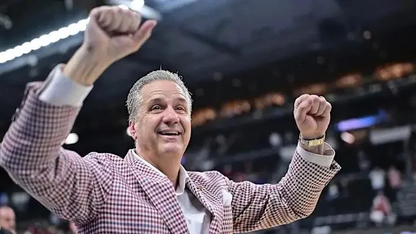 Basketball coach in a red plaid sport coat raising both fists in celebration in an arena