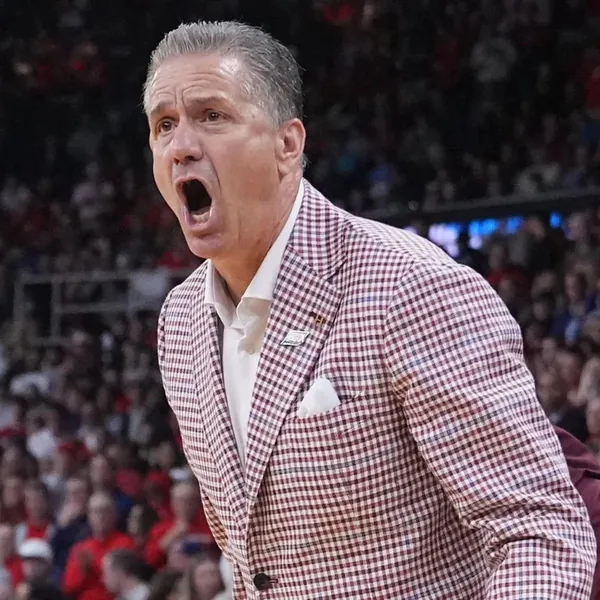 Basketball coach in a red plaid sport coat calling out on the sideline in front of a packed crowd