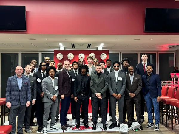 Basketball team and staff in suits posing together for a group photo in a red-walled room