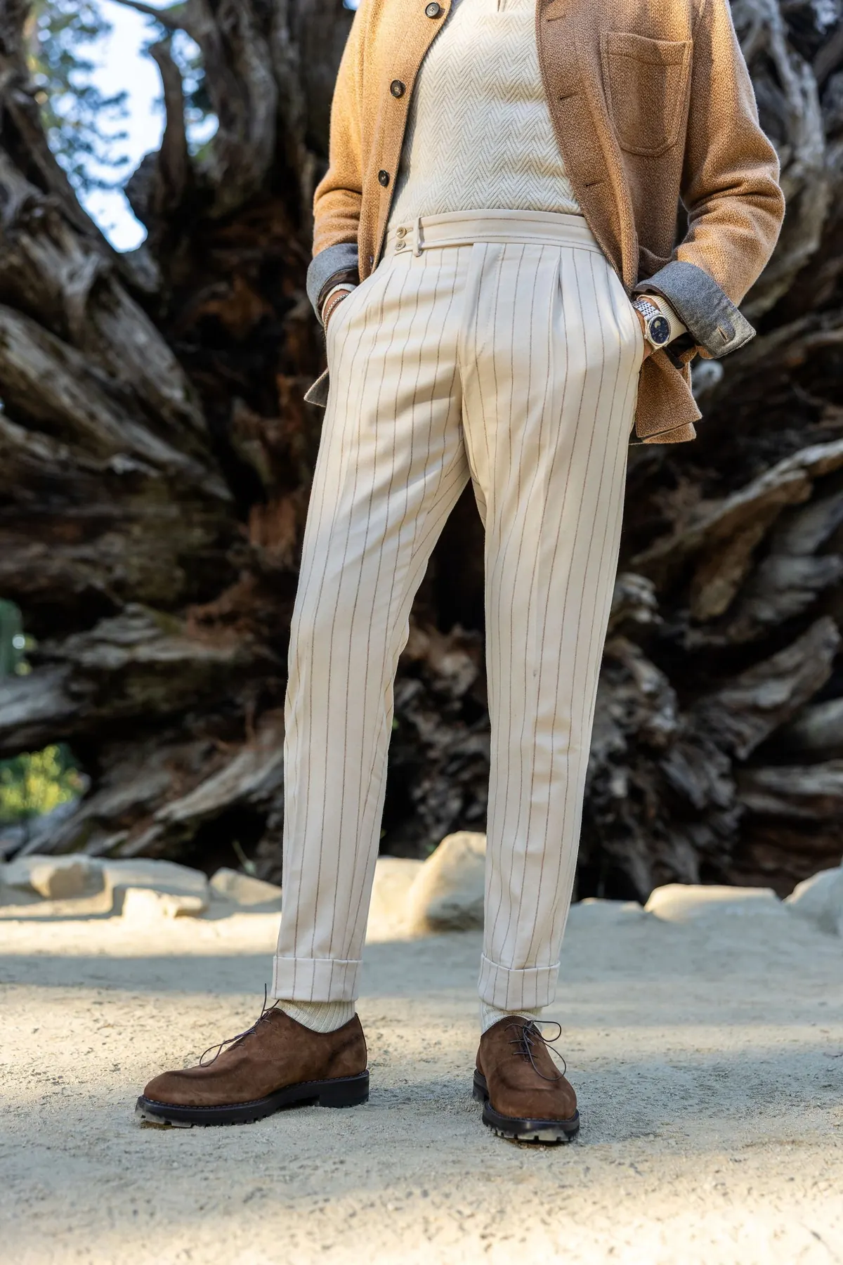 Cream pinstriped pleated trousers, a camel jacket and brown leather shoes, photographed in front of the upturned roots of a fallen sequoia