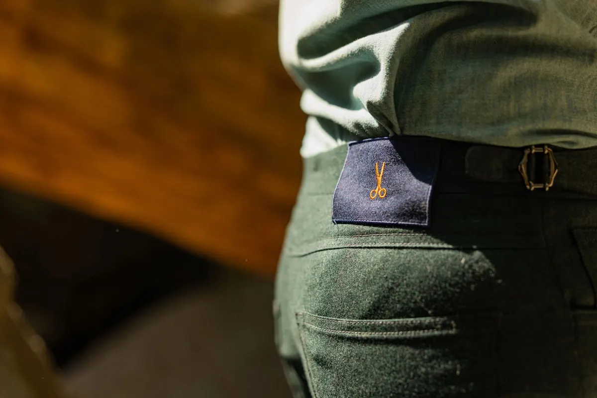 Close-up of the back pocket of green wool trousers with a leather patch and a buckled side adjuster
