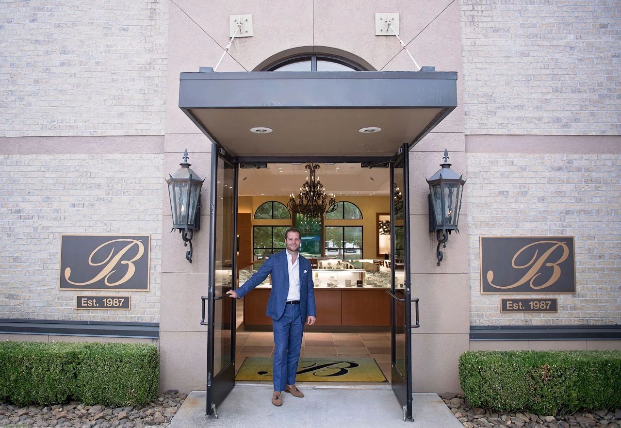 Man in blue suit welcoming at open doors.