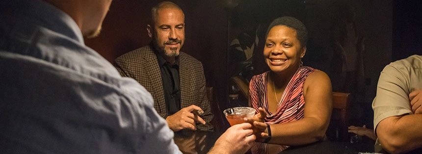 Two people sharing drinks and smiling in a dimly lit setting.